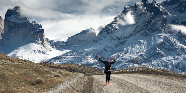 Corredora celebrando en un camino de ripio con las montañas nevadas de Torres del Paine al fondo